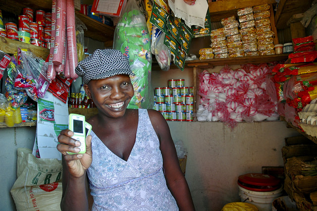 A Haitian female drug shop seller holds up a mobile phone